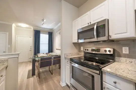 kitchen with natural light, stainless steel microwave, electric range oven, white cabinets, light granite-like countertops, and light parquet floors