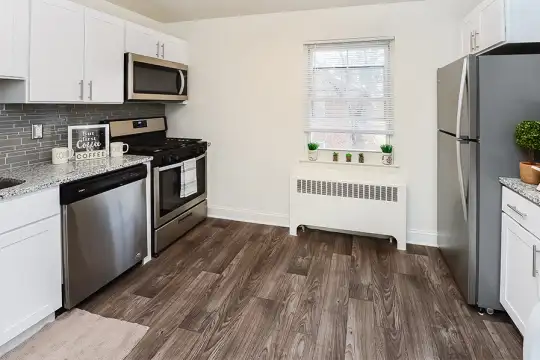 kitchen featuring natural light, radiator, gas range oven, stainless steel appliances, white cabinets, light granite-like countertops, and dark hardwood flooring