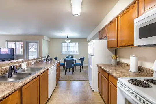 kitchen featuring natural light, refrigerator, dishwasher, TV, microwave, light tile floors, pendant lighting, light granite-like countertops, and brown cabinetry