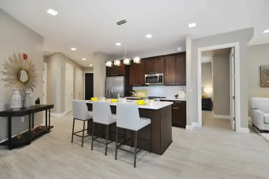 kitchen featuring stainless steel appliances, light flooring, light countertops, kitchen island sink, dark brown cabinetry, and pendant lighting