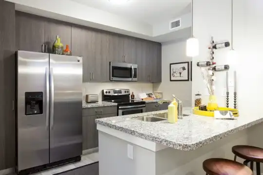 kitchen featuring a breakfast bar area, stainless steel appliances, electric range oven, light floors, pendant lighting, light granite-like countertops, and dark brown cabinets