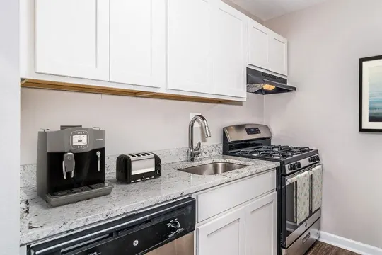 kitchen featuring ventilation hood, dishwasher, gas range oven, white cabinetry, light floors, and light stone countertops
