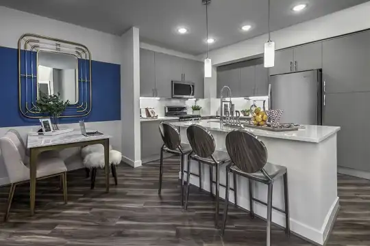 kitchen with a breakfast bar area, stainless steel refrigerator, microwave, range oven, light countertops, kitchen island sink, dark hardwood floors, pendant lighting, and white cabinets