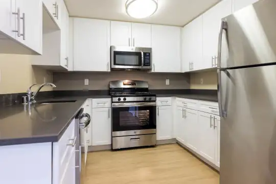 kitchen featuring gas range oven, stainless steel appliances, dark countertops, white cabinetry, and light parquet floors