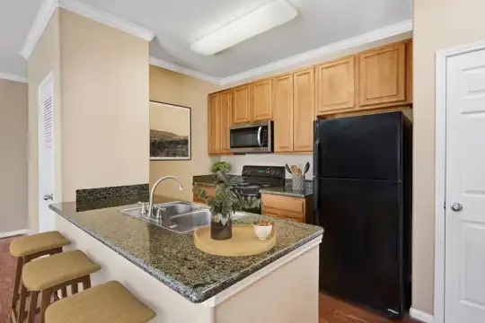 kitchen with a kitchen bar, stainless steel microwave, refrigerator, range oven, dark stone countertops, brown cabinets, and light parquet floors
