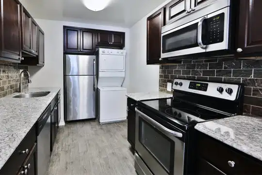 kitchen with stainless steel appliances, washer / dryer, electric range oven, light stone countertops, dark brown cabinetry, and light hardwood floors