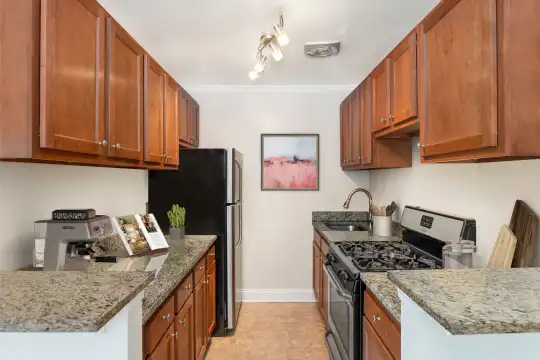 kitchen featuring refrigerator, gas range oven, light granite-like countertops, light tile floors, and brown cabinetry
