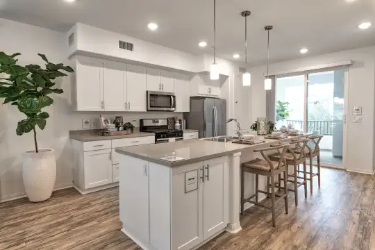 kitchen featuring natural light, a breakfast bar area, stainless steel appliances, range oven, pendant lighting, white cabinets, light parquet floors, and an island with sink