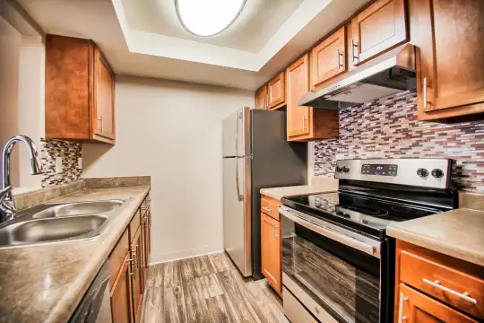kitchen featuring range hood, refrigerator, electric range oven, dishwasher, light countertops, light hardwood floors, and brown cabinetry