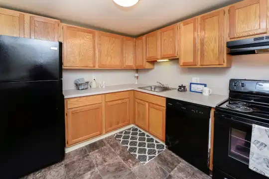 kitchen featuring electric range oven, refrigerator, extractor fan, dishwasher, light countertops, dark tile flooring, and brown cabinetry