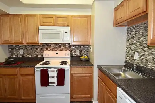 kitchen featuring electric range oven, dishwasher, microwave, dark granite-like countertops, and brown cabinets