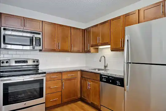 kitchen featuring stainless steel appliances, electric range oven, brown cabinets, light flooring, and light granite-like countertops