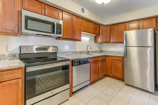 kitchen featuring stainless steel appliances, electric range oven, light tile floors, brown cabinets, and light granite-like countertops