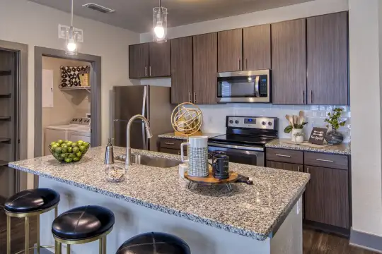 kitchen featuring a kitchen bar, a center island, washer / dryer, electric range oven, stainless steel appliances, dark brown cabinetry, light granite-like countertops, pendant lighting, and dark hardwood flooring