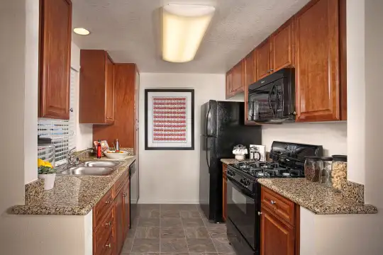 kitchen featuring refrigerator, gas range oven, dishwasher, microwave, dark granite-like countertops, brown cabinets, and dark tile floors