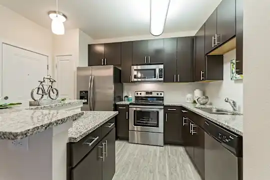 kitchen featuring a center island, electric range oven, stainless steel appliances, dark brown cabinetry, light hardwood floors, pendant lighting, and light stone countertops
