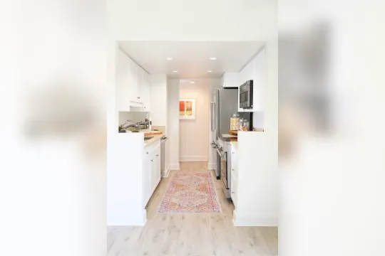 kitchen with stainless steel microwave, dishwasher, range oven, light countertops, white cabinetry, and light parquet floors