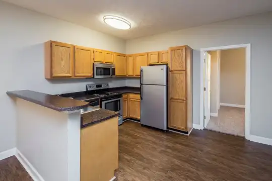 kitchen with refrigerator, range oven, microwave, dark stone countertops, brown cabinetry, and dark hardwood flooring