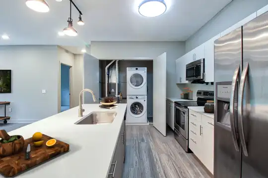 kitchen with independent washer and dryer, electric range oven, stainless steel appliances, white cabinetry, pendant lighting, light hardwood floors, light countertops, and kitchen island sink