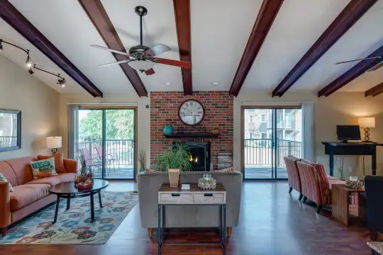 hardwood floored living room featuring a wealth of natural light, a ceiling fan, a brick fireplace, vaulted ceiling with beams, and TV