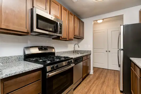 kitchen with refrigerator, gas range oven, dishwasher, stainless steel microwave, light stone countertops, light parquet floors, and light brown cabinets