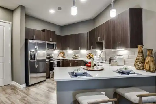 kitchen with a breakfast bar area, stainless steel refrigerator, range oven, microwave, pendant lighting, light flooring, dark brown cabinetry, and light countertops