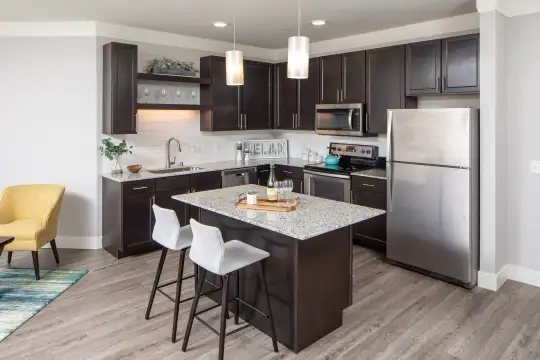kitchen featuring a kitchen breakfast bar, stainless steel appliances, electric range oven, pendant lighting, dark brown cabinetry, light granite-like countertops, and light hardwood floors