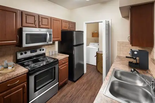 kitchen with stainless steel microwave, washer / dryer, refrigerator, electric range oven, light granite-like countertops, brown cabinets, and dark hardwood floors