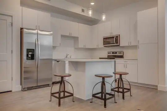 kitchen featuring a breakfast bar area, stainless steel appliances, range oven, white cabinets, light countertops, pendant lighting, and light hardwood flooring