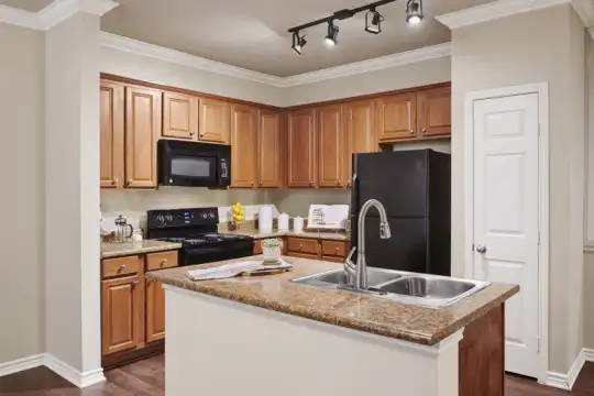 kitchen with refrigerator, microwave, range oven, granite-like countertops, dark parquet floors, a center island with sink, and brown cabinetry