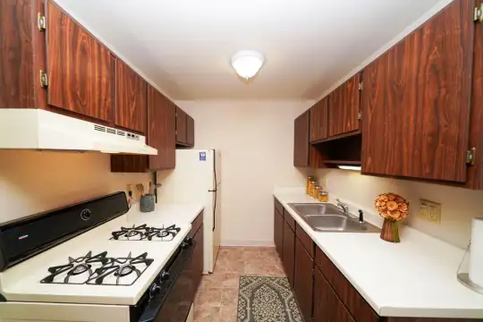 kitchen with gas cooktop, ventilation hood, refrigerator, light tile floors, light countertops, and dark brown cabinets