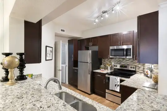 kitchen with a breakfast bar area, stainless steel appliances, electric range oven, light hardwood floors, light stone countertops, and dark brown cabinets
