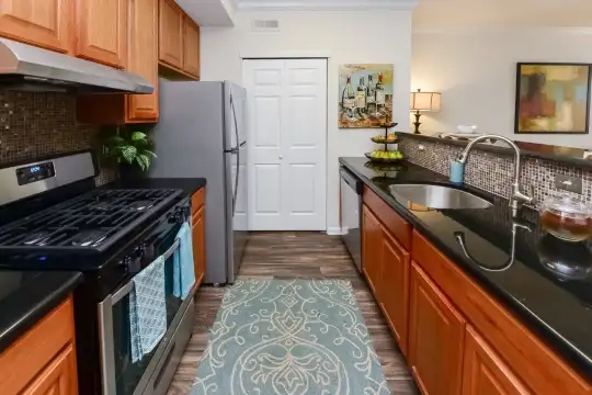 kitchen featuring exhaust hood, gas range oven, dishwasher, dark flooring, dark granite-like countertops, and brown cabinets