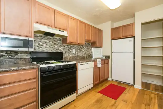 kitchen featuring refrigerator, fume extractor, stainless steel microwave, dishwasher, gas range oven, light hardwood flooring, light brown cabinets, and dark stone countertops
