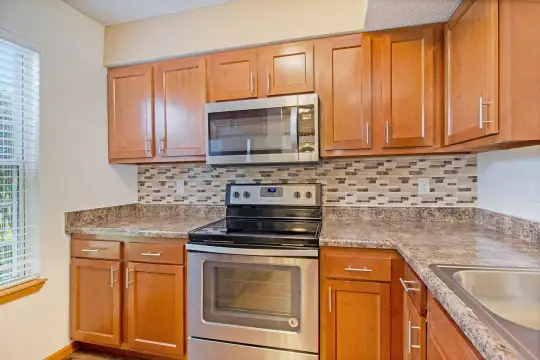 kitchen with electric range oven, stainless steel microwave, granite-like countertops, light floors, and brown cabinetry