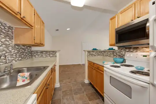kitchen with stainless steel microwave, electric range oven, light countertops, dark tile floors, and light brown cabinets