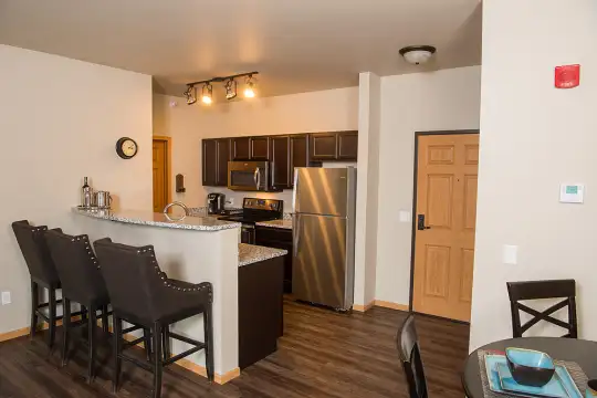 kitchen featuring hardwood floors, a kitchen bar, stainless steel refrigerator, range oven, microwave, granite-like countertops, and dark brown cabinets