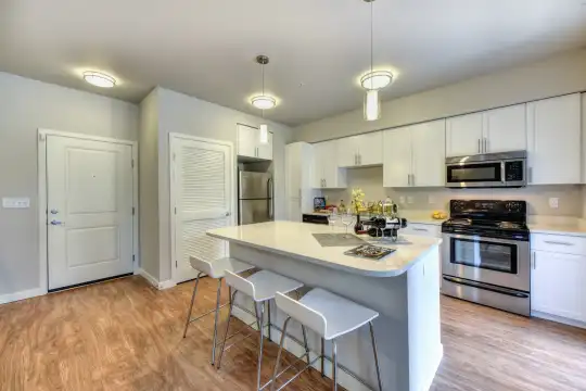 kitchen featuring a kitchen bar, stainless steel appliances, range oven, white cabinets, light countertops, pendant lighting, and light hardwood flooring