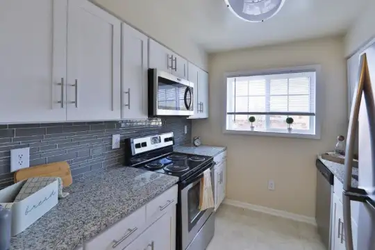 kitchen with natural light, refrigerator, dishwasher, electric range oven, stainless steel microwave, light tile floors, white cabinets, and light granite-like countertops