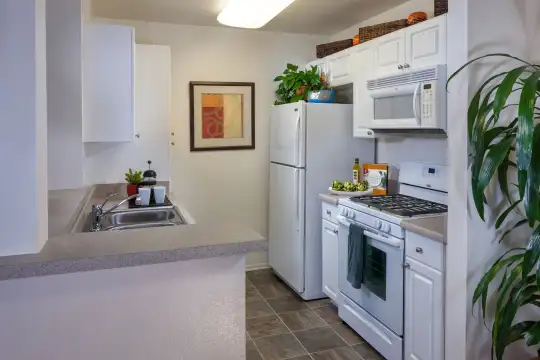 kitchen featuring refrigerator, gas range oven, microwave, white cabinetry, dark tile flooring, and light stone countertops