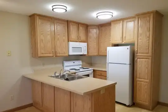 kitchen with refrigerator, electric range oven, microwave, light countertops, light hardwood floors, and brown cabinets
