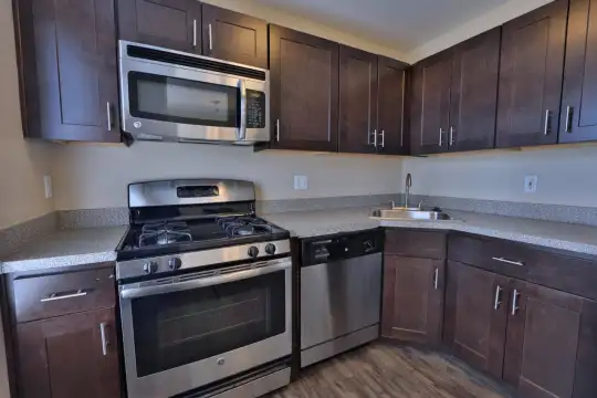 kitchen with stainless steel appliances, gas range oven, dark hardwood floors, light granite-like countertops, and dark brown cabinets