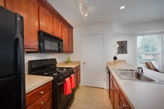 kitchen featuring natural light, gas range oven, refrigerator, microwave, light countertops, light tile floors, and brown cabinets