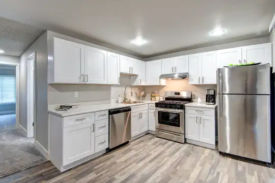 kitchen with natural light, gas range oven, stainless steel appliances, fume extractor, white cabinets, light countertops, and light hardwood flooring