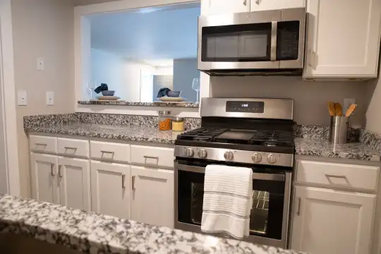 kitchen with gas range oven, stainless steel microwave, white cabinetry, and light granite-like countertops