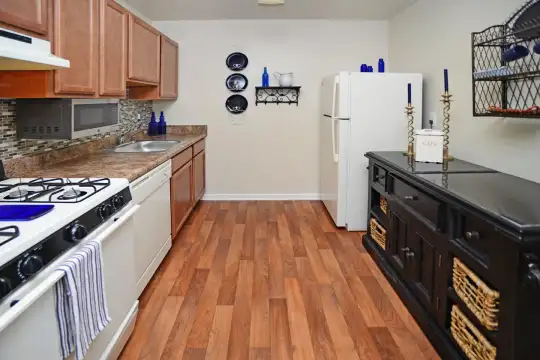 kitchen featuring ventilation hood, gas range oven, dishwasher, refrigerator, microwave, dark brown cabinetry, dark stone countertops, and light hardwood flooring