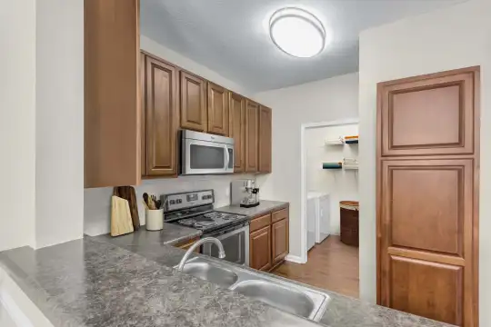 kitchen featuring electric range oven, stainless steel microwave, granite-like countertops, light parquet floors, and brown cabinets