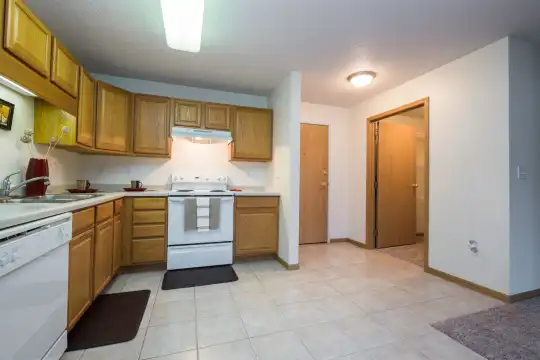 kitchen featuring dishwasher, electric range oven, fume extractor, light tile floors, light countertops, and brown cabinetry