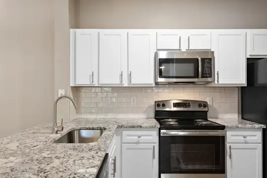 kitchen featuring stainless steel microwave, refrigerator, electric range oven, white cabinets, and light granite-like countertops