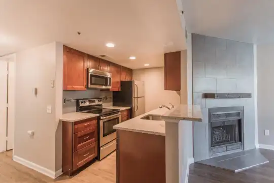 kitchen featuring a fireplace, refrigerator, electric range oven, stainless steel microwave, light hardwood flooring, light stone countertops, and brown cabinets